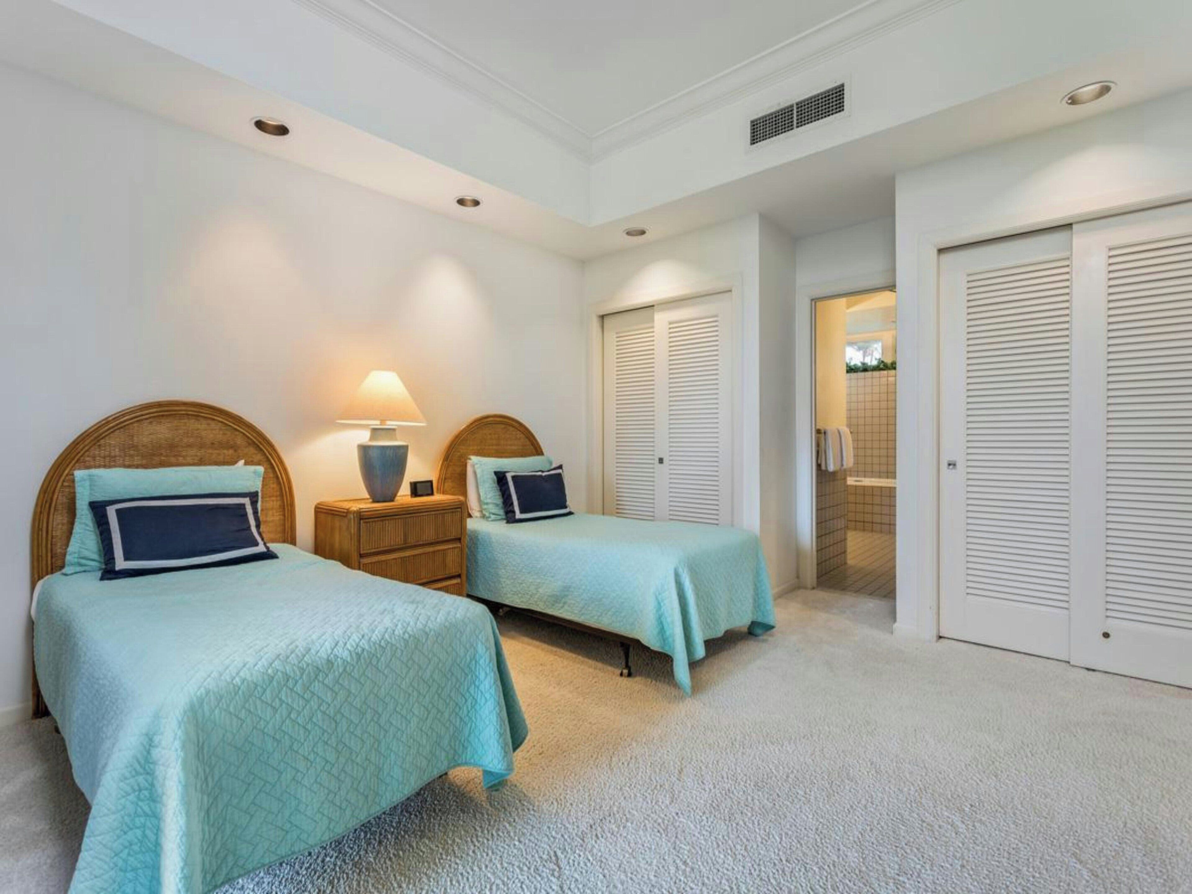A bedroom with two beds, a nightstand with a lamp, a walk-in closet, and a bathroom visible through an open door.
