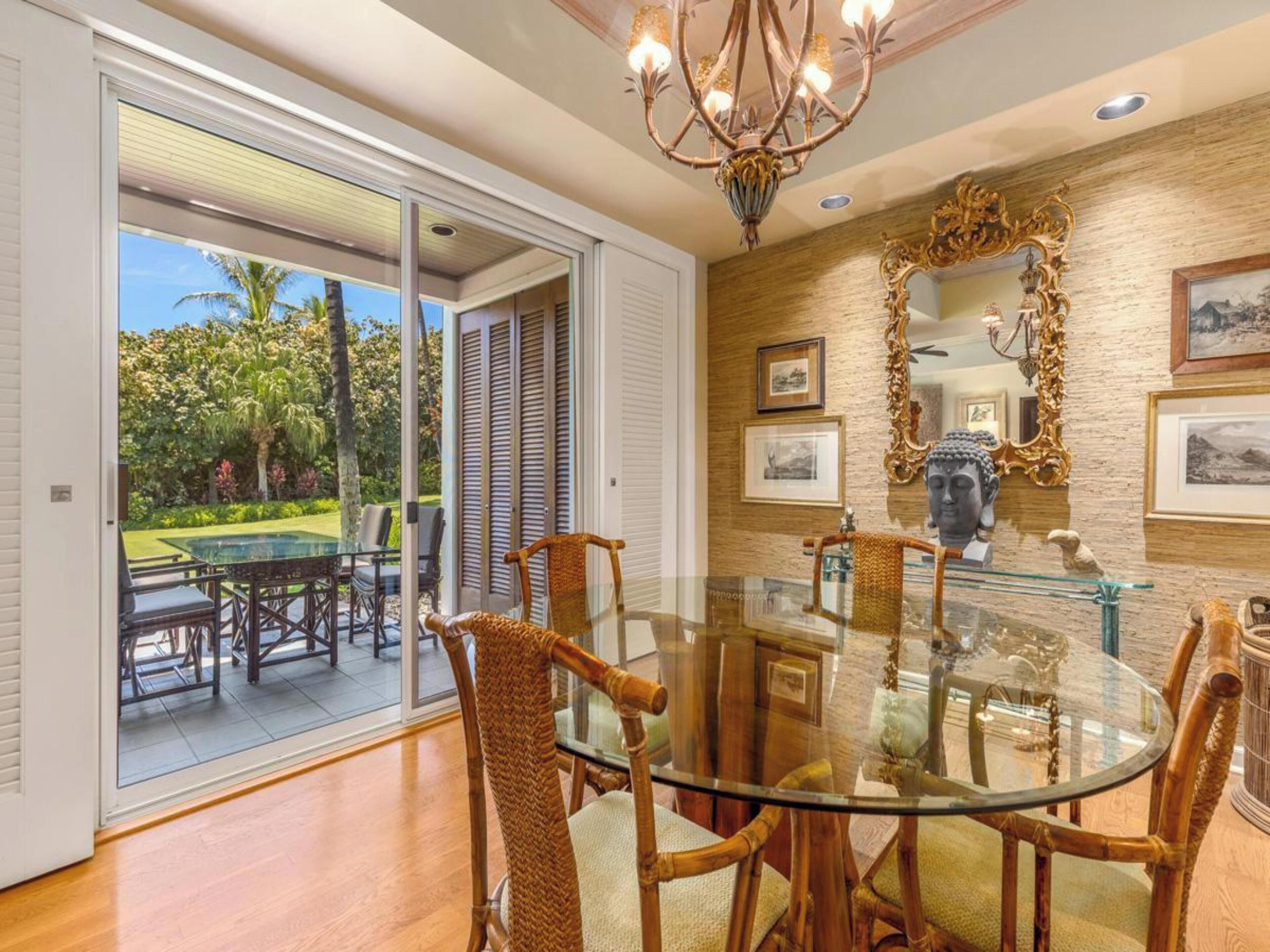 A dining area with a glass table and wicker chairs, a chandelier, and a view of the outdoors.