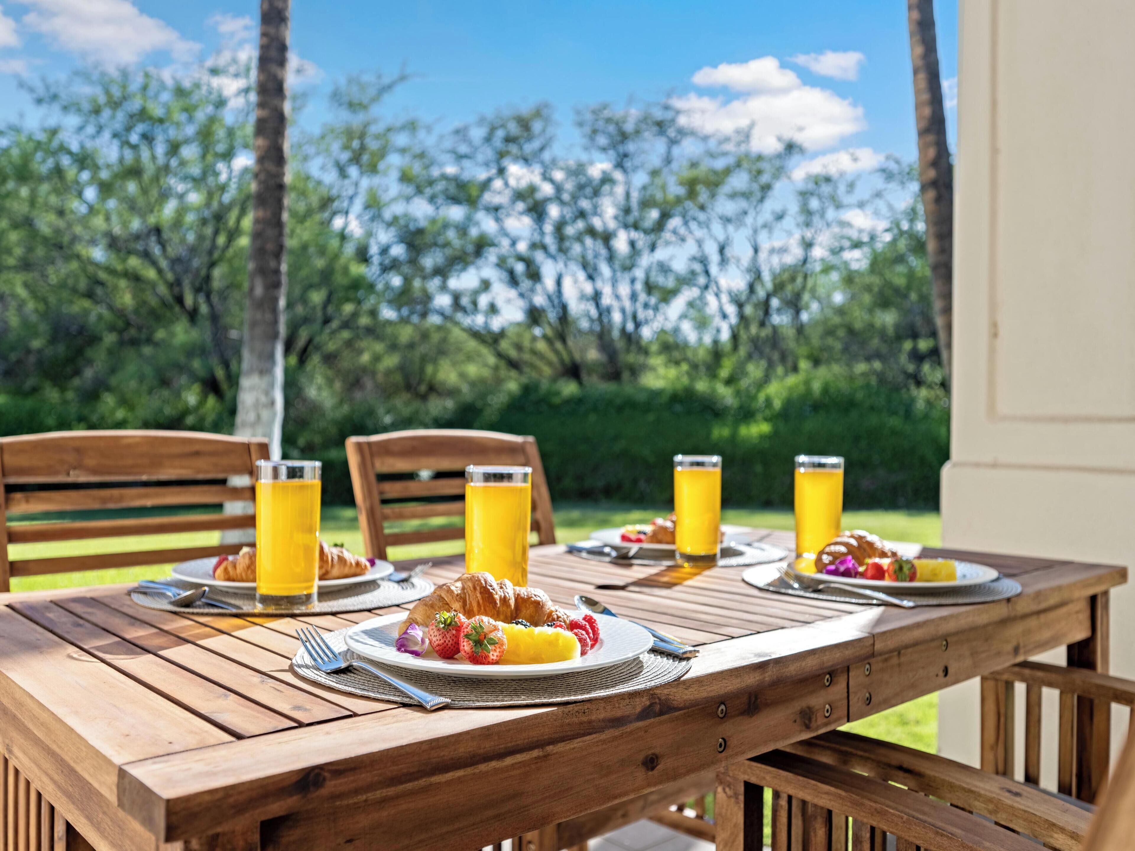 Mesa de madera preparada para el desayuno, con cruasanes, fresas y vasos de jugo.
