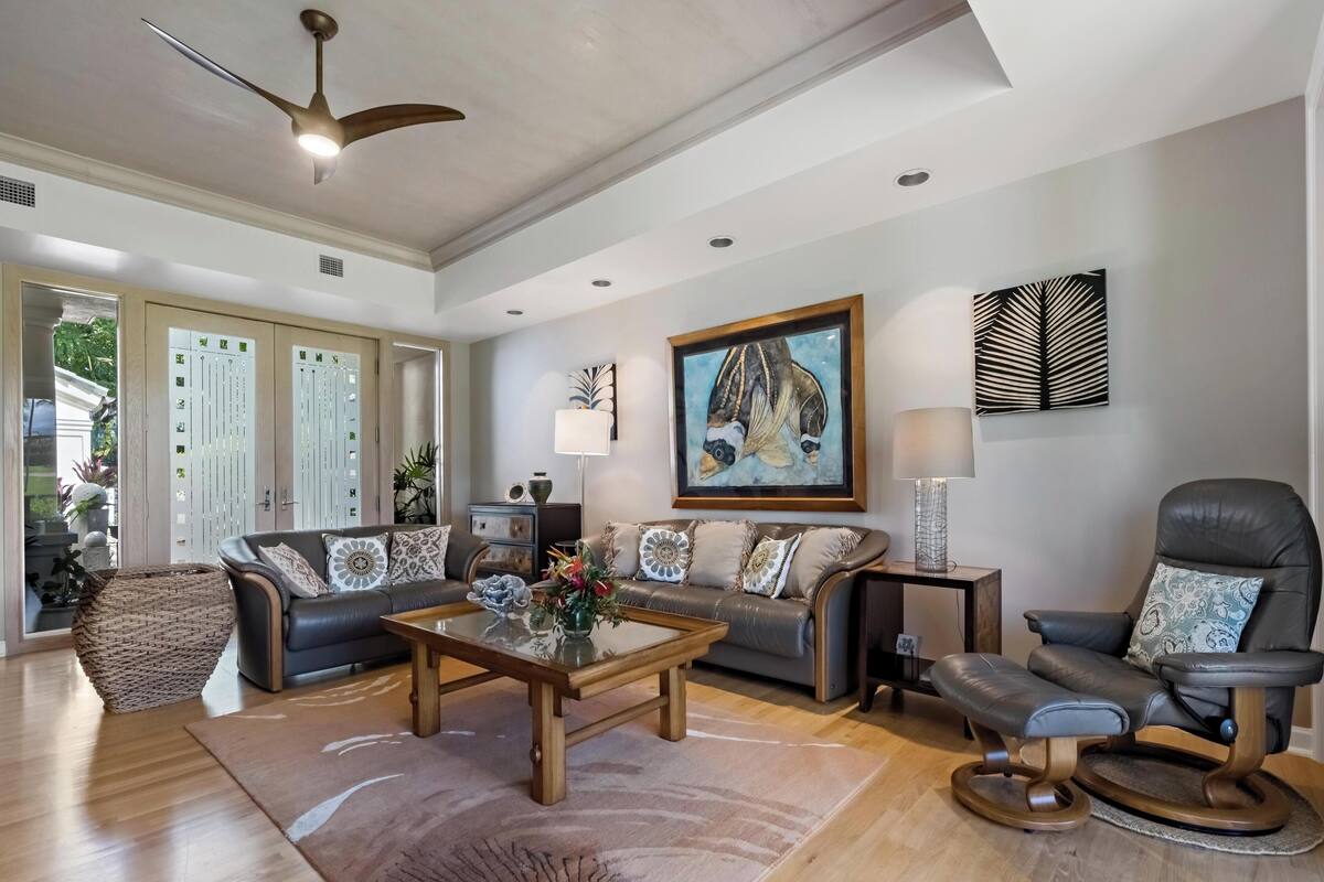 A spacious living room with a modern ceiling fan, a large painting, and a leather armchair.