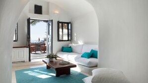 Een moderne woonkamer met een witte bank, turquoise kussens, een houten salontafel en uitzicht op de natuur door een open deur.