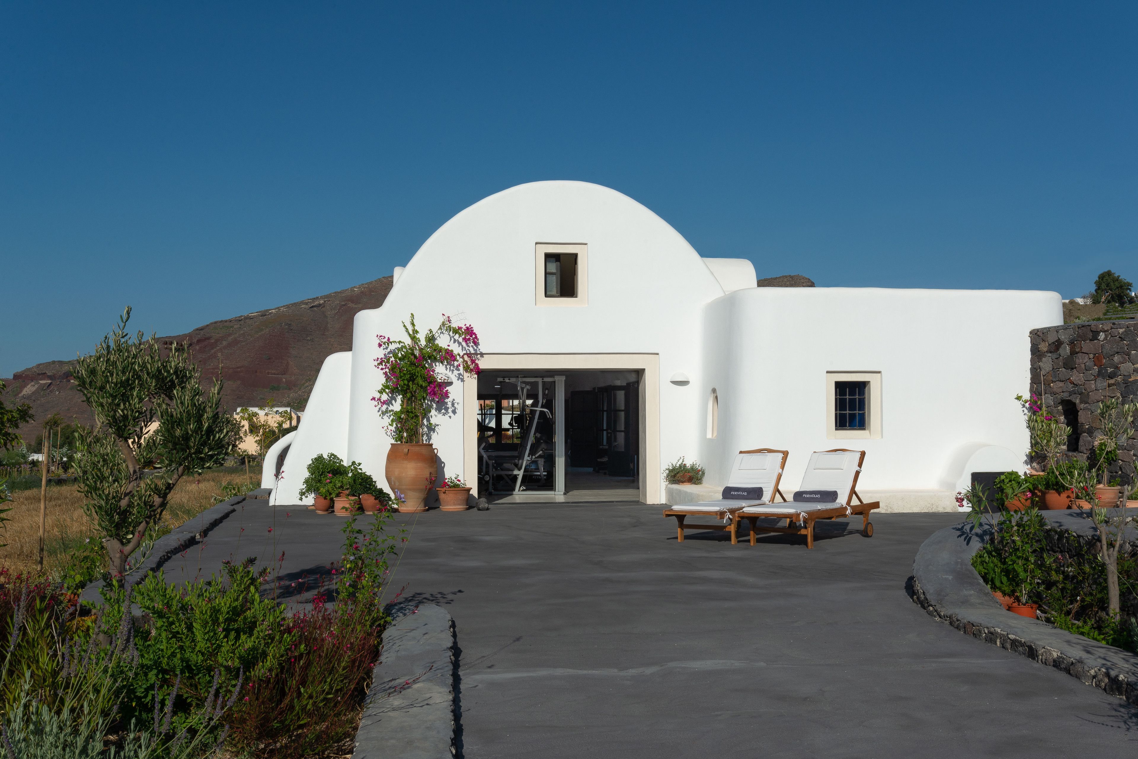 A white building with a curved roof, a small window, and a door. There are two lounge chairs outside.