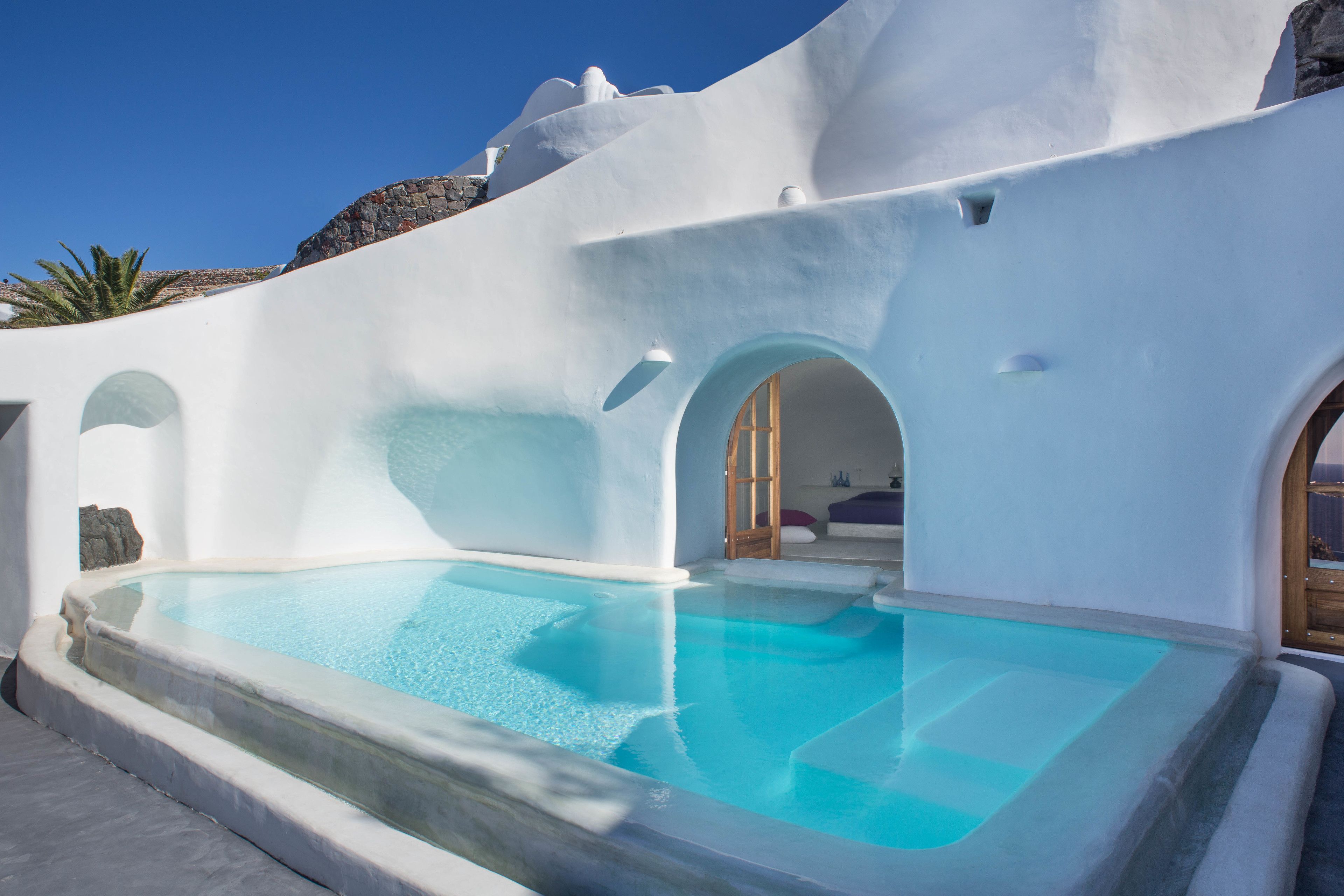 Un edificio moderno de color blanco con piscina, arcos y una pared de piedra.