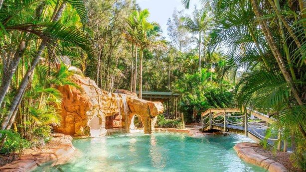 A natural pool with a rock formation, surrounded by tropical vegetation. - BreakFree Aanuka Beach Resort (Coffs Harbour)