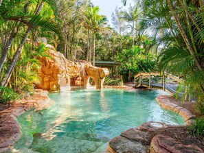 A natural pool with a rock formation, surrounded by tropical vegetation. - BreakFree Aanuka Beach Resort (Coffs Harbour)