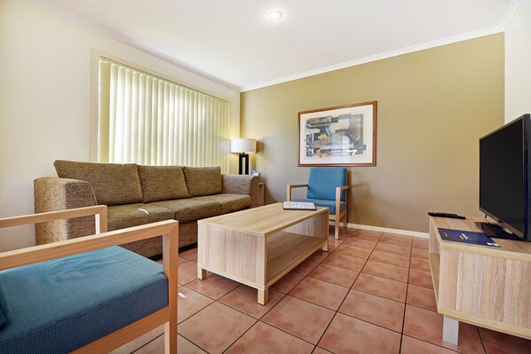 A living room with a sofa, a coffee table, a TV, and a painting on the wall. - BreakFree Aanuka Beach Resort (Coffs Harbour)