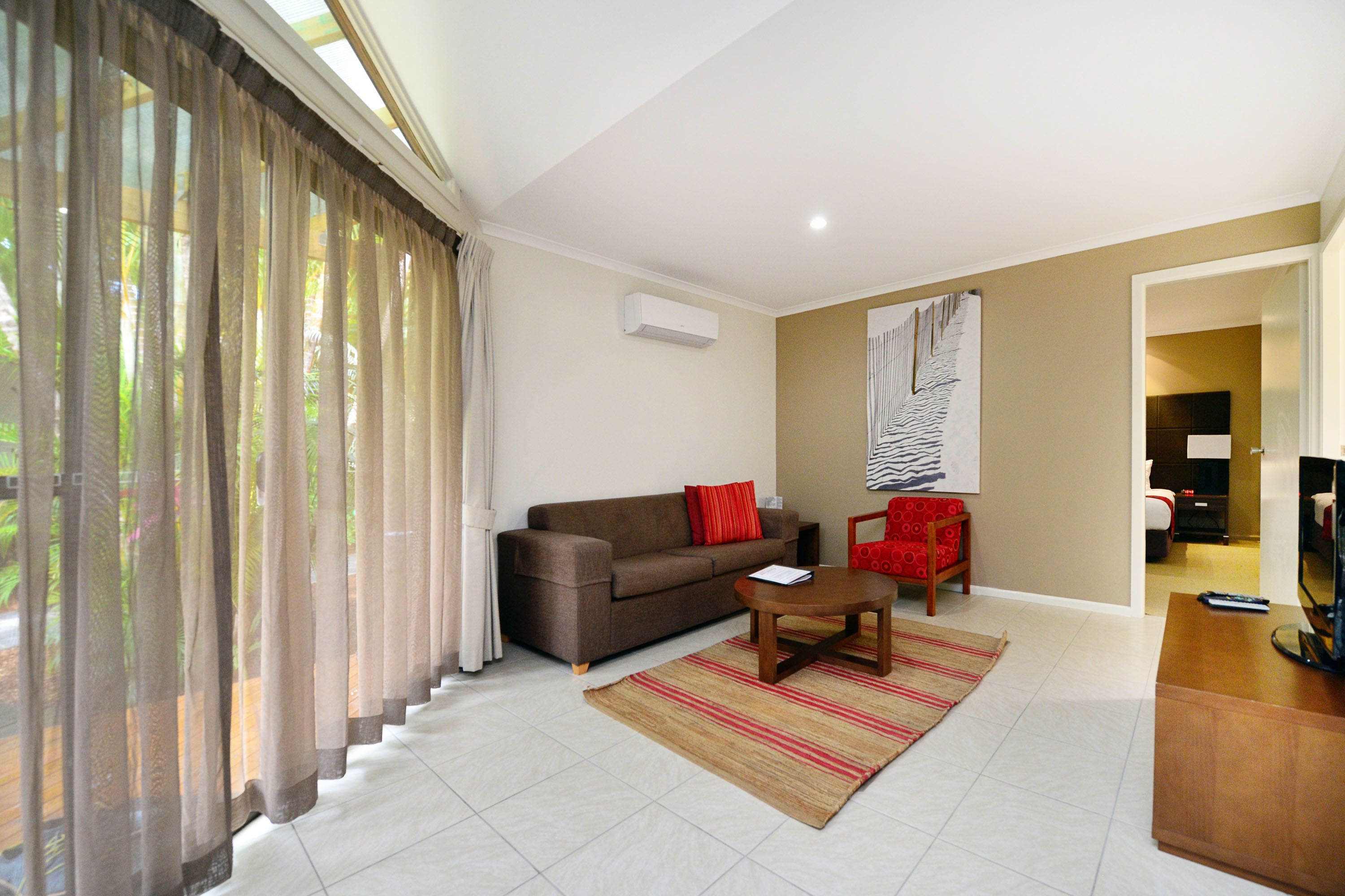 A living room with a sofa, a coffee table, a TV, and a red chair.