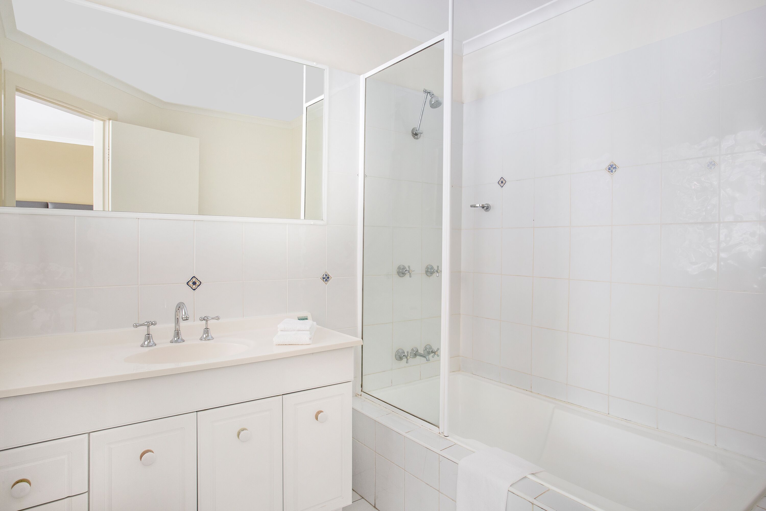 A modern bathroom with a white vanity, a glass shower enclosure, and a large mirror.