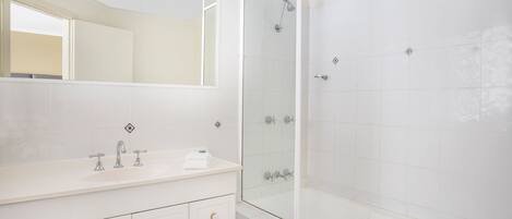 A modern bathroom with a white vanity, a glass shower enclosure, and a large mirror.