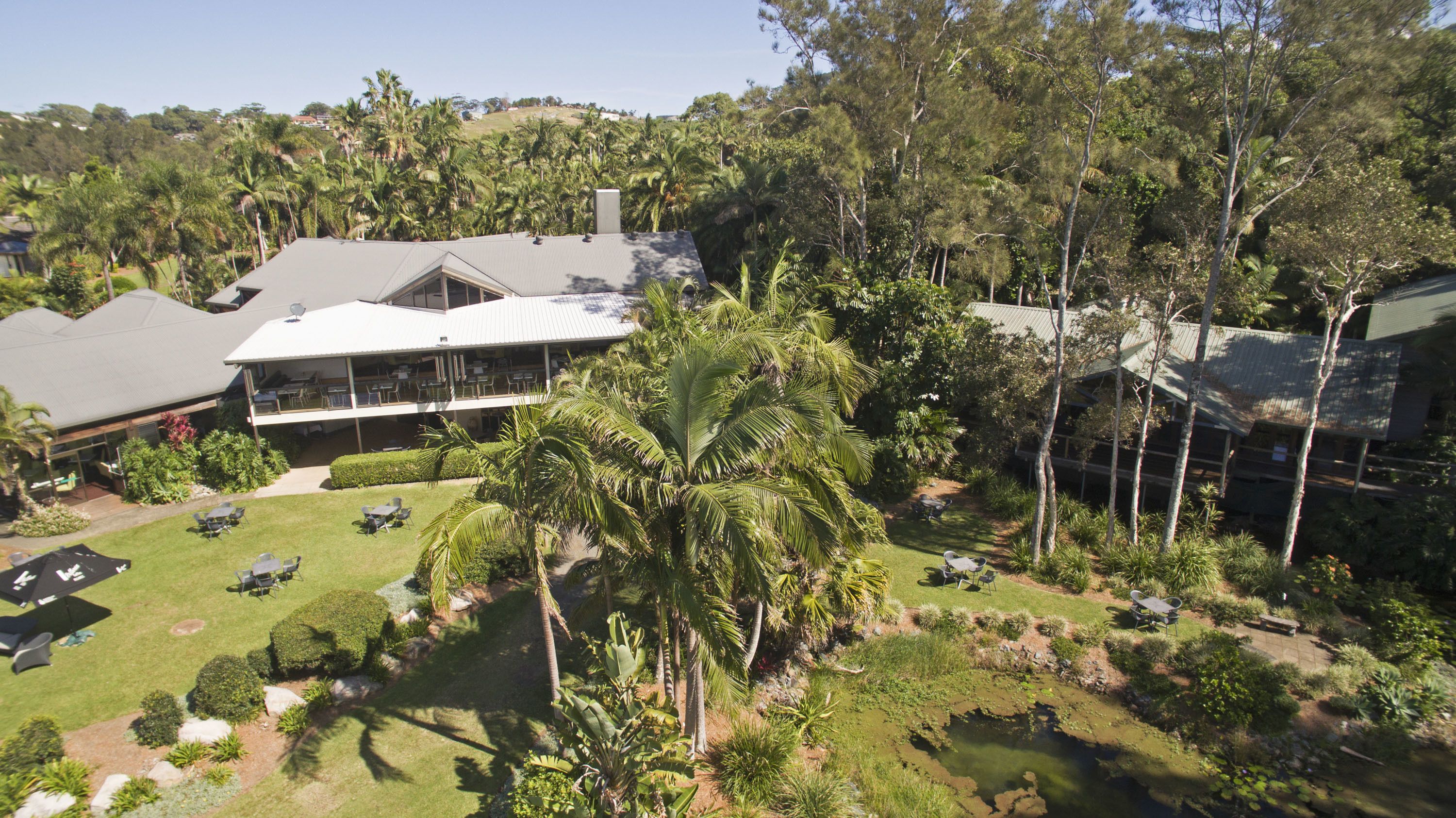 A hotel with a large, multi-level structure, outdoor seating areas, and a lush garden with palm trees.