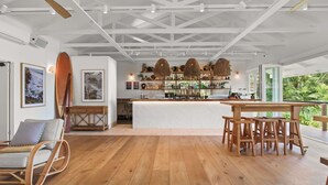 A spacious room with a wooden floor, a bar area with a white countertop, and a ceiling fan. - BreakFree Aanuka Beach Resort (Coffs Harbour)