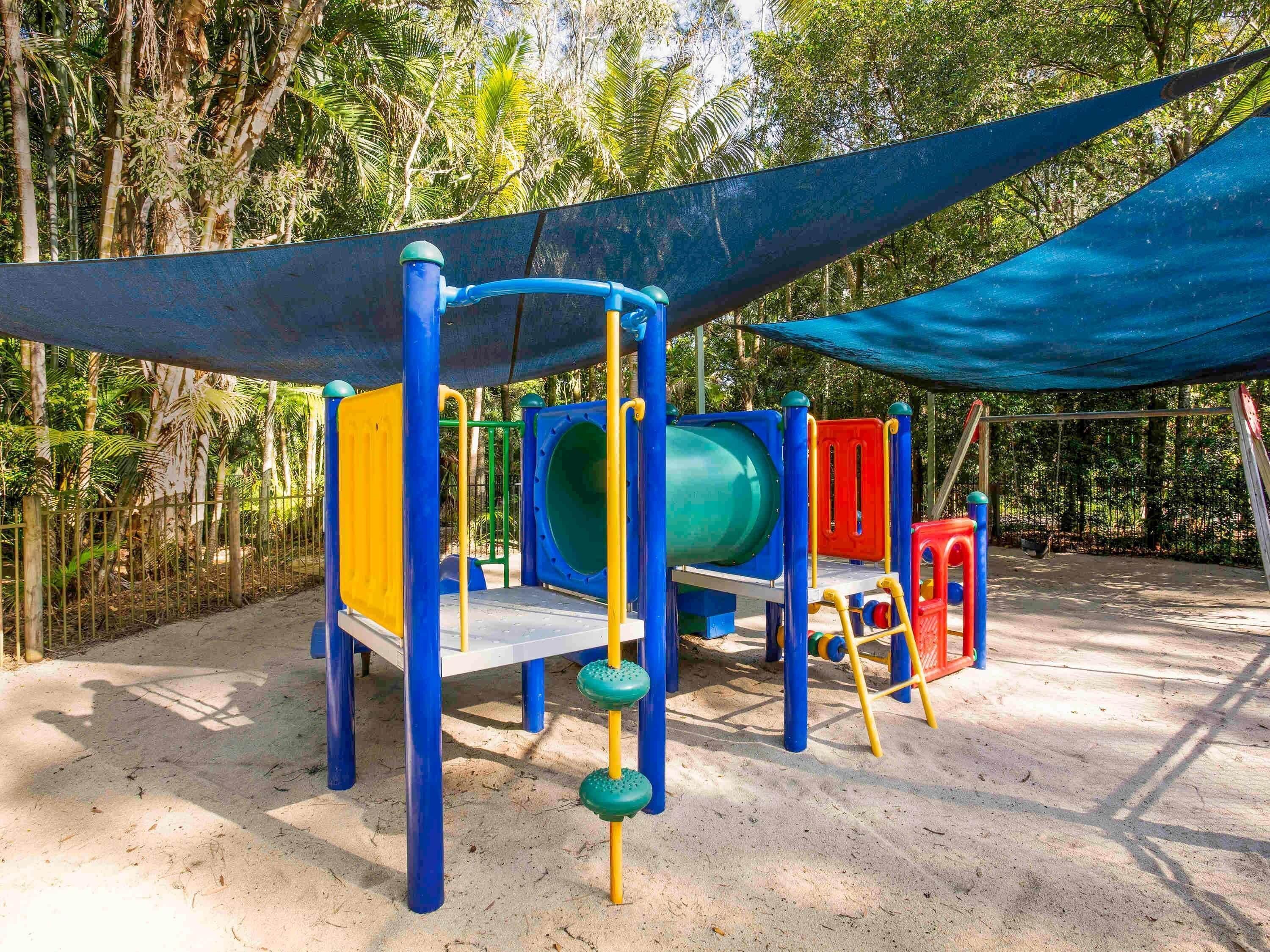 A playground with a slide, climbing structures, and a shaded area.