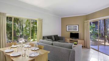 A living room with a sofa, TV, dining table set, and large windows with curtains.