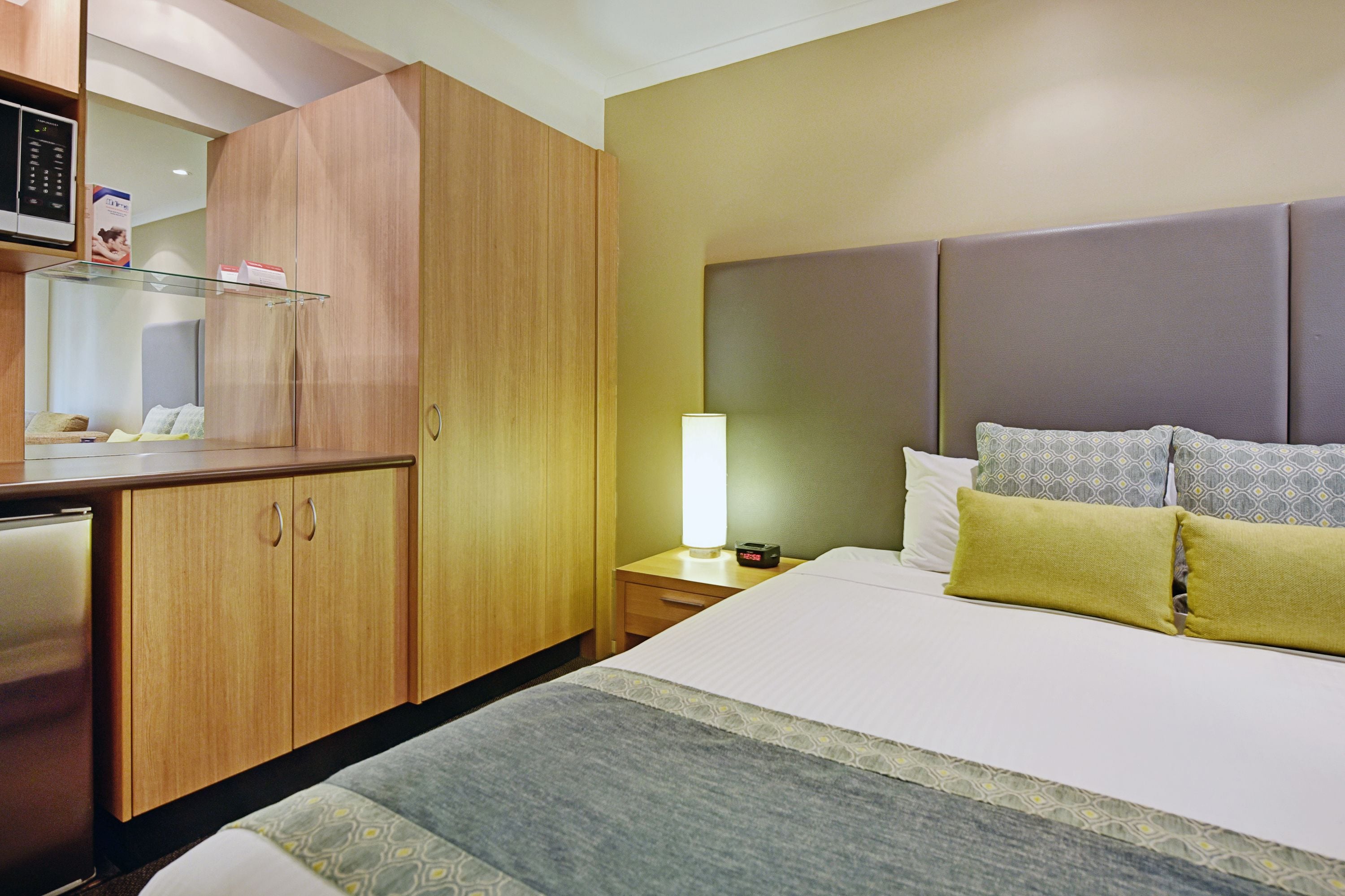 Une chambre d’hôtel avec un lit, une table de chevet, une lampe et une armoire en bois.
