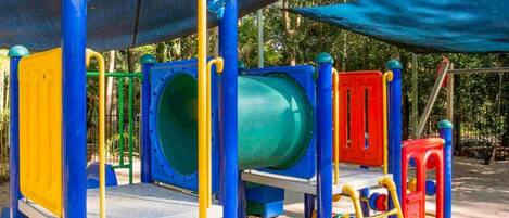 Un parque infantil con diversas estructuras de juego, incluyendo toboganes, escaleras de cuerda y columpios.