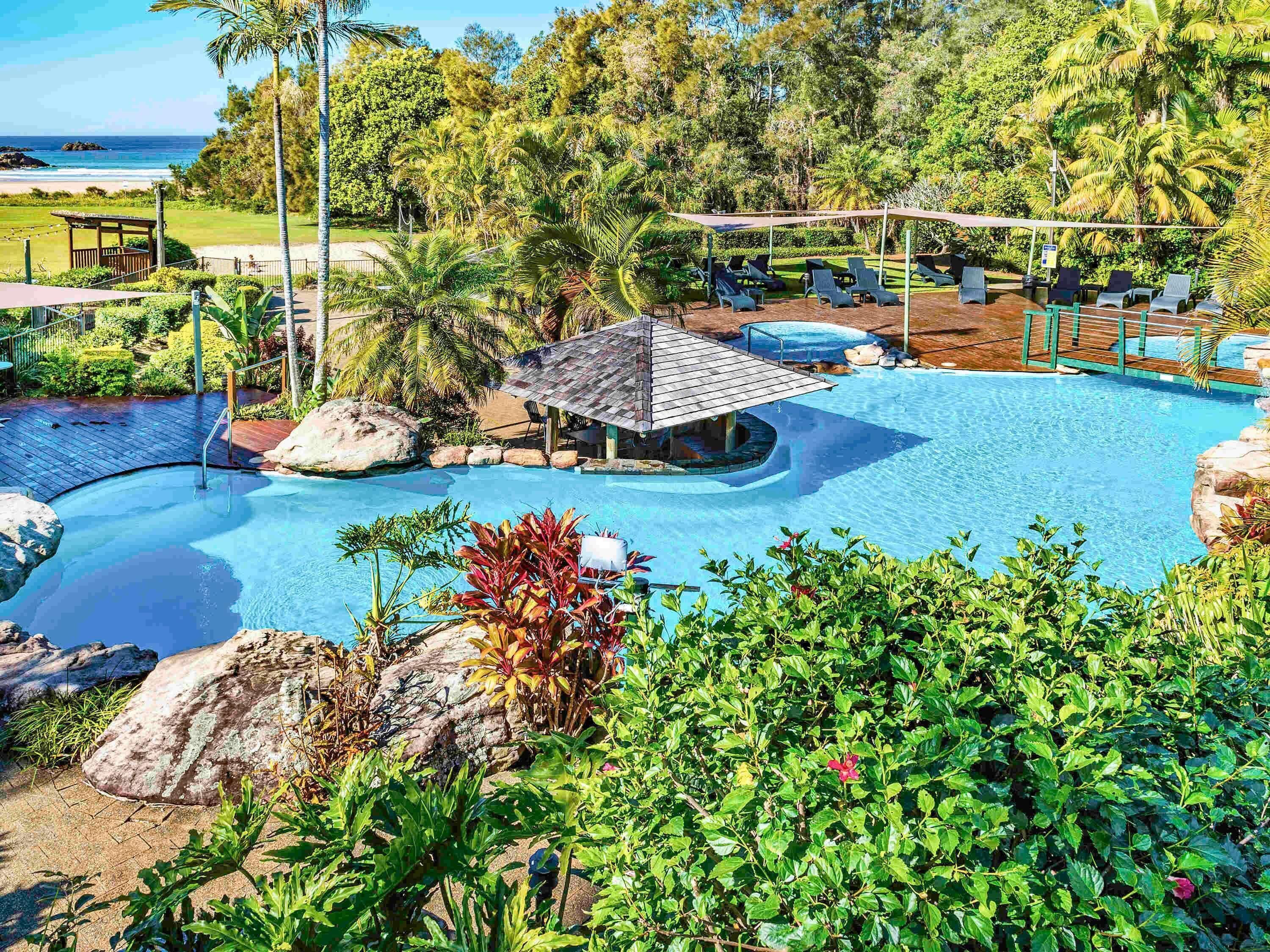 Een zwembad van een resort met ligbedden, een klein paviljoen en tropische begroeiing.