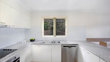A modern kitchen with white cabinets, a built-in stove, a dishwasher, and a window with a view of greenery.