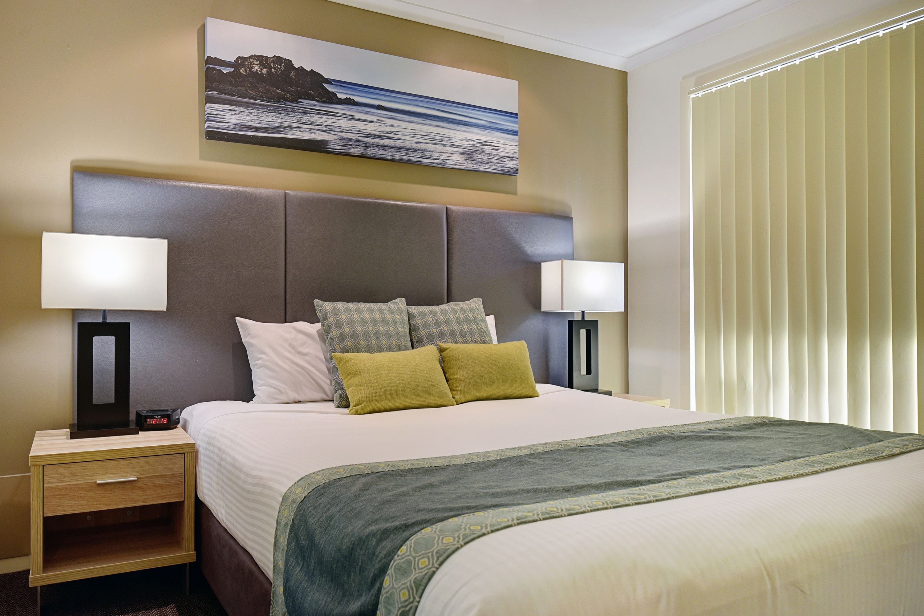 Een hotelkamer met een groot bed, twee nachtkastjes, een wandlamp en een raam met zonwering.