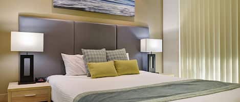 Een hotelkamer met een groot bed, twee nachtkastjes, een wandlamp en een raam met zonwering.