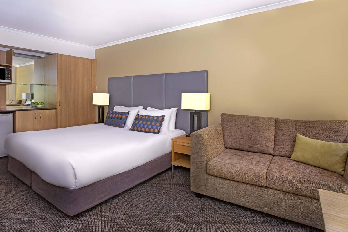 Ein Hotelzimmer mit Bett, Sofa, Nachttisch und Spiegel.