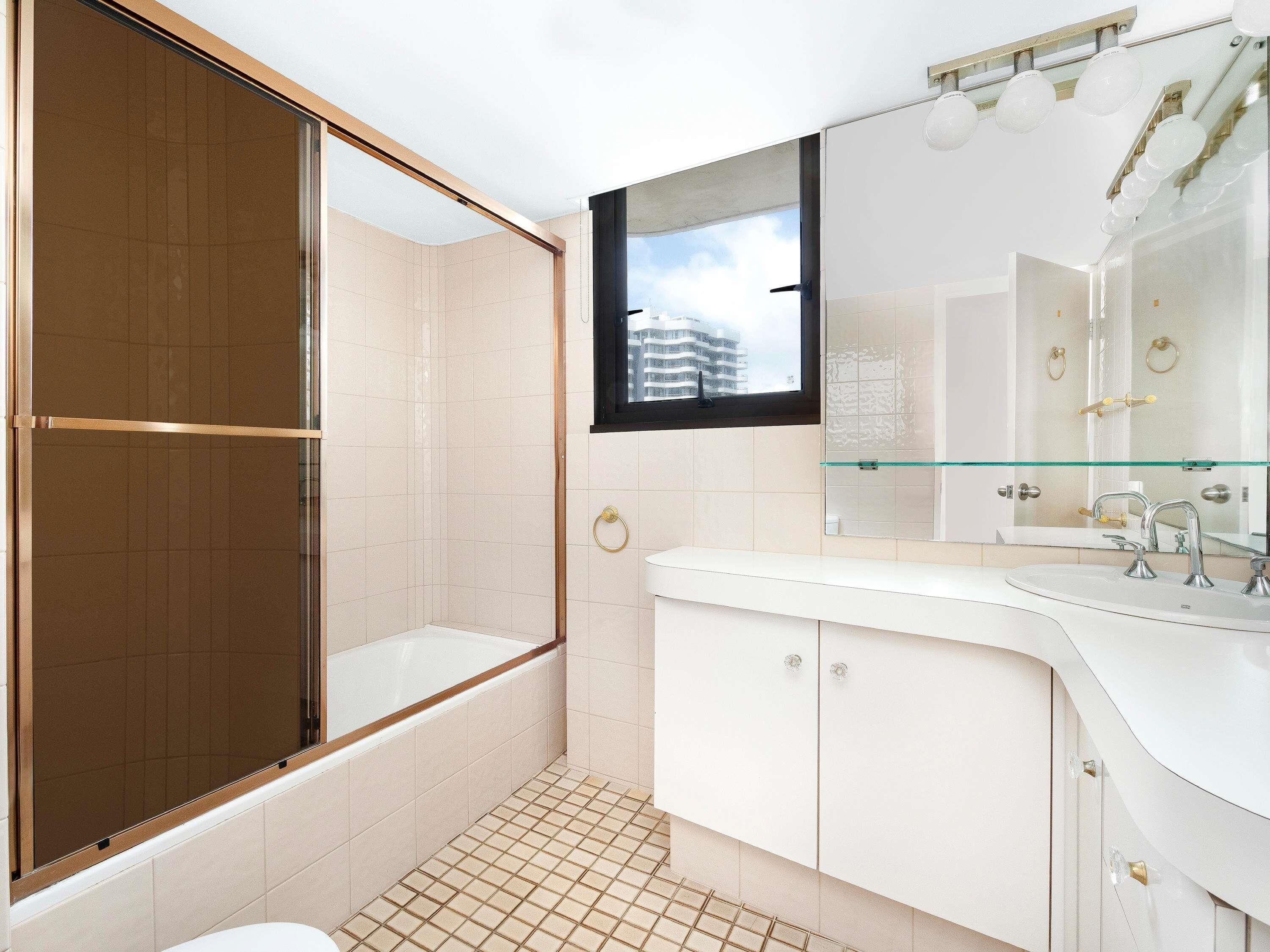 A modern bathroom with a glass shower enclosure, a white vanity with a mirror, and a view of buildings outside.