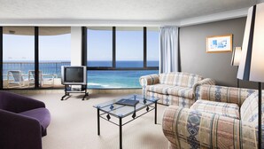 Una habitación con un ventanal grande que da al océano, televisión, sofá y mesa de centro.