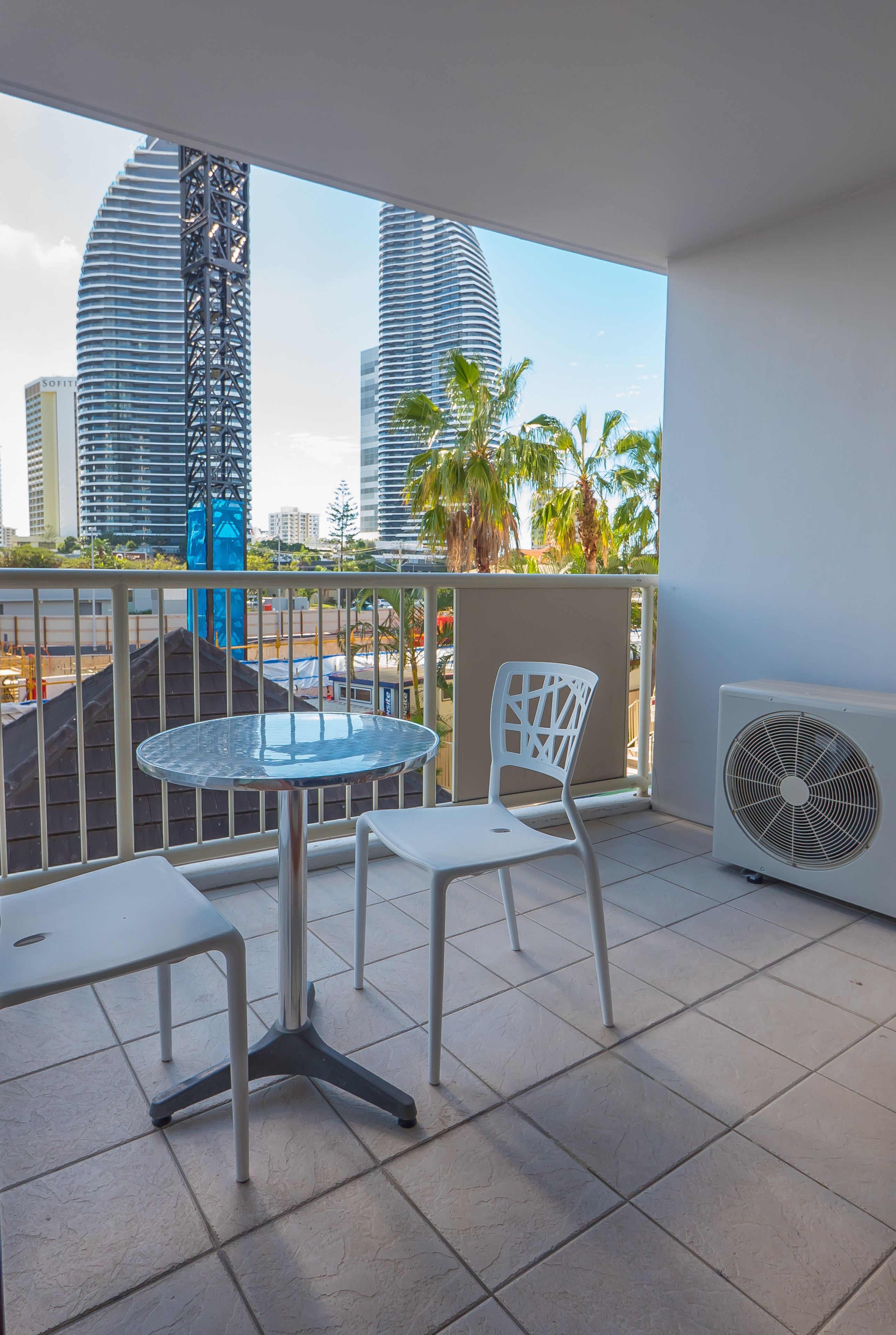 Un balcone con un tavolo rotondo e due sedie, vista su edifici moderni e palme.