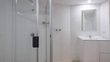 A modern bathroom with a glass shower enclosure, a sink with a mirror, and white tiled walls.