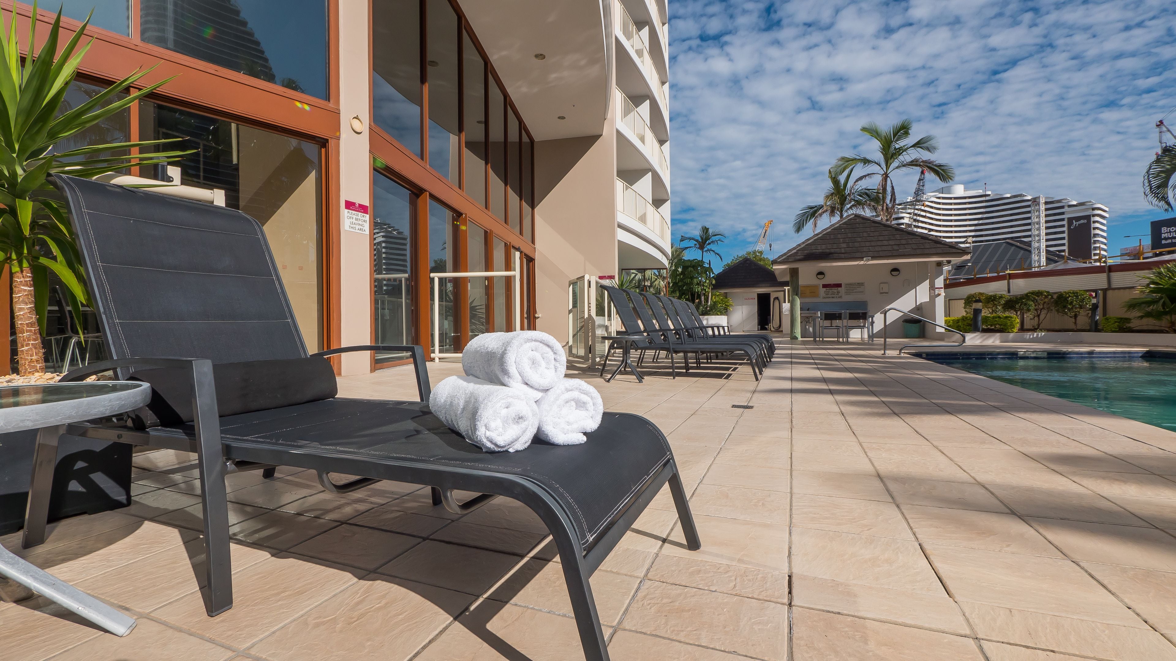 A poolside area with lounge chairs, a stack of towels, and a building with a sign indicating a restricted area.