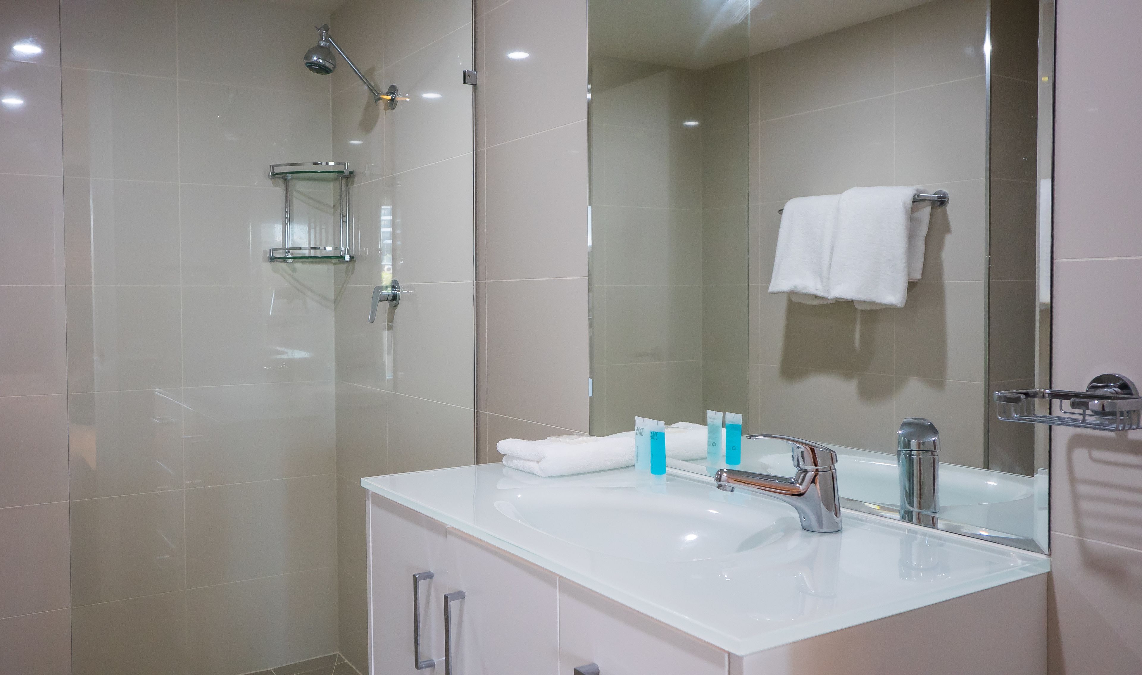Un baño moderno con cabina de ducha de vidrio, un lavabo blanco con espejo y un perchero para toallas.