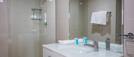 Un baño moderno con cabina de ducha de vidrio, un lavabo blanco con espejo y un perchero para toallas.