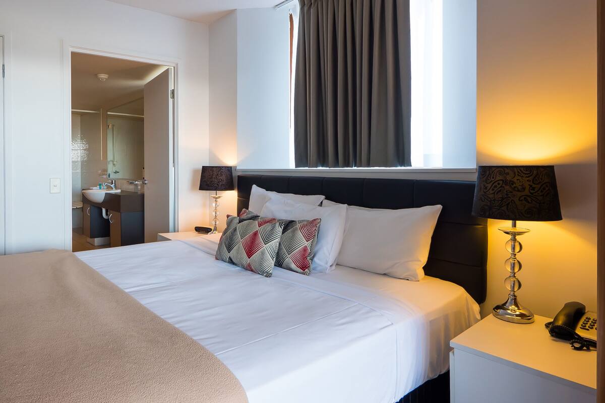Een hotelkamer met een bed, bedlampen, een telefoon en een raam met gordijnen.