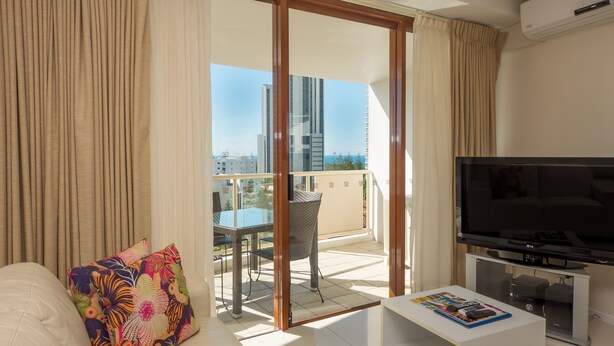 Un salon moderne doté d’un téléviseur à écran plat, d’un canapé et d’un balcon avec une porte vitrée.