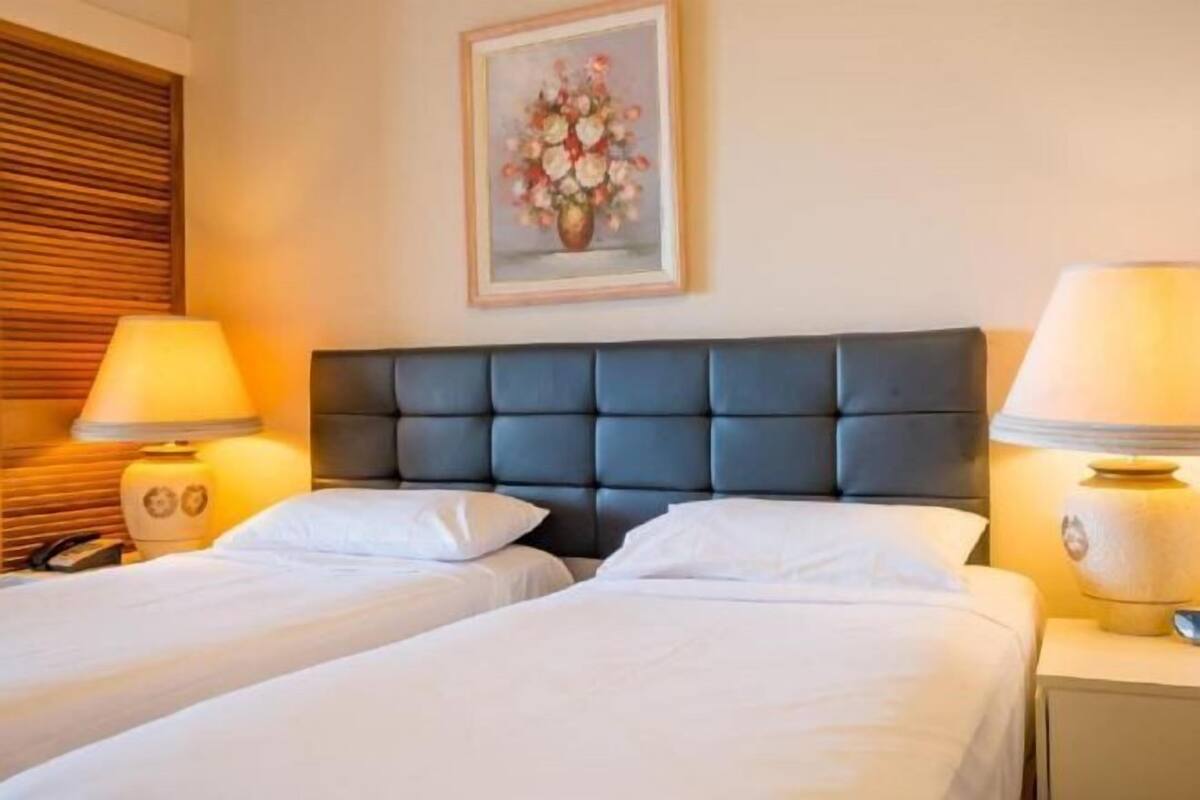 Hotelkamer met twee bedden, een donker hoofdeinde, bedlampen, een lijst met bloemkunst aan de muur, en een houten hoofdeinde aan de linkerkant.