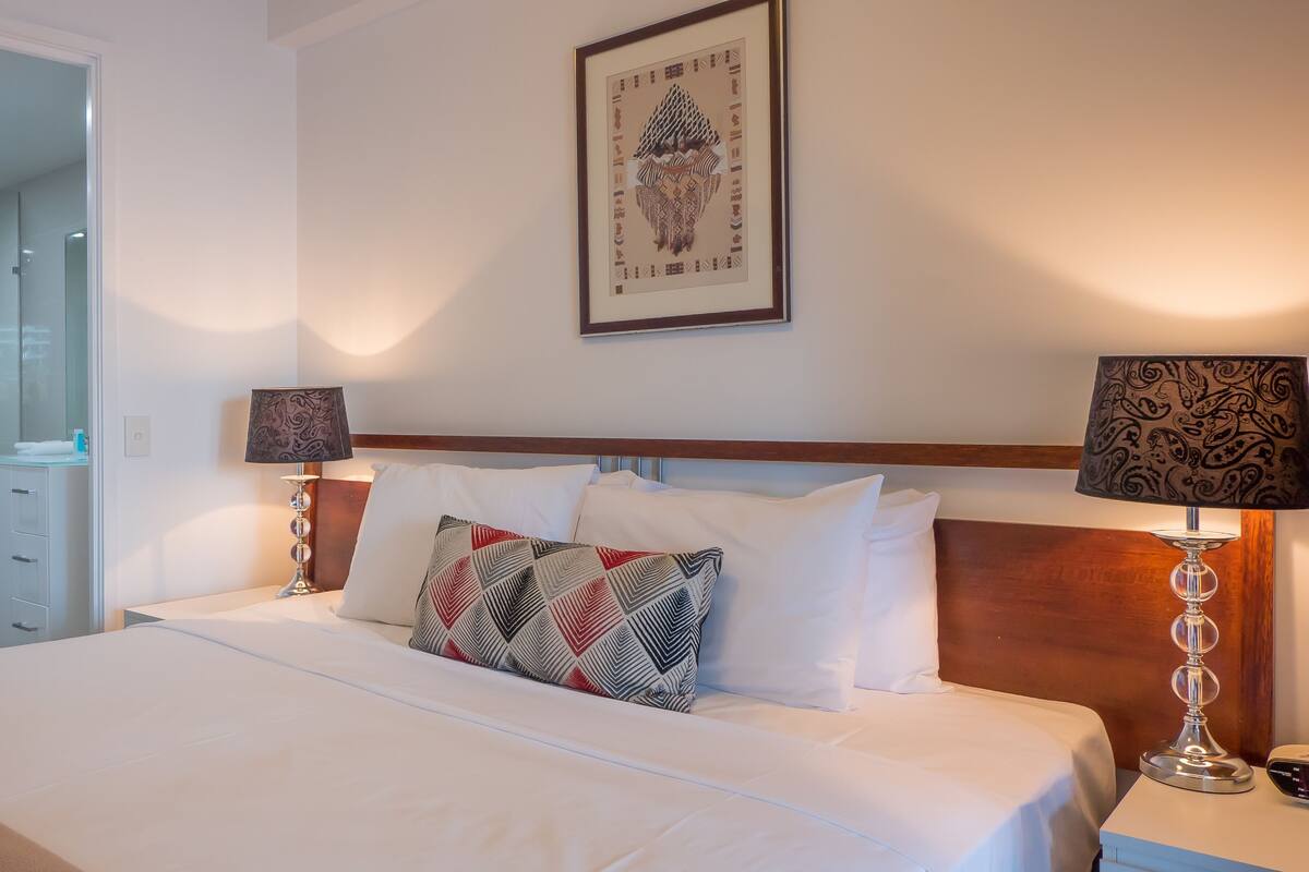 Hotelkamer met een groot bed, twee bedlampen, een lijst met kunstwerk aan de muur en een douchecabine van glas.