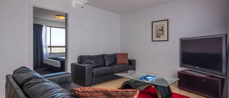 A modern living room with a black leather sofa, a glass coffee table, and a flat-screen TV.
