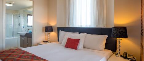 A hotel room with a bed, bedside lamps, a telephone, and a bathroom visible through an open door.