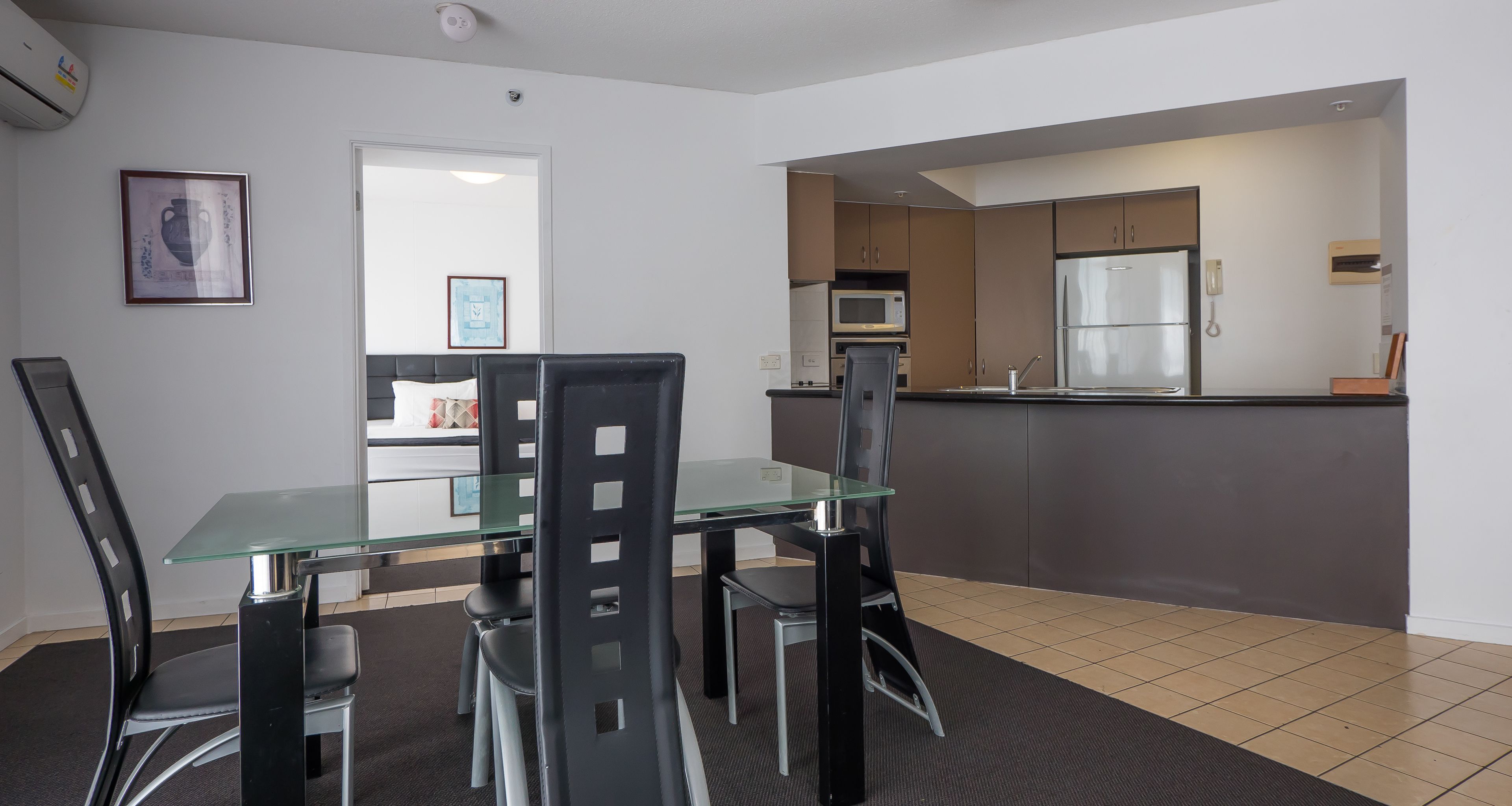 Een moderne keuken met roestvrijstalen apparatuur, een glazen eettafel en zwarte stoelen.