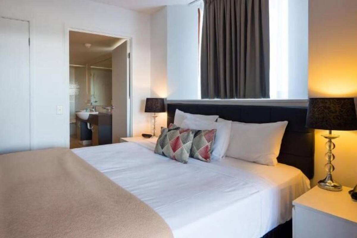 Een hotelkamer met een bed, nachtkastjes, een lamp en een raam met gordijnen.