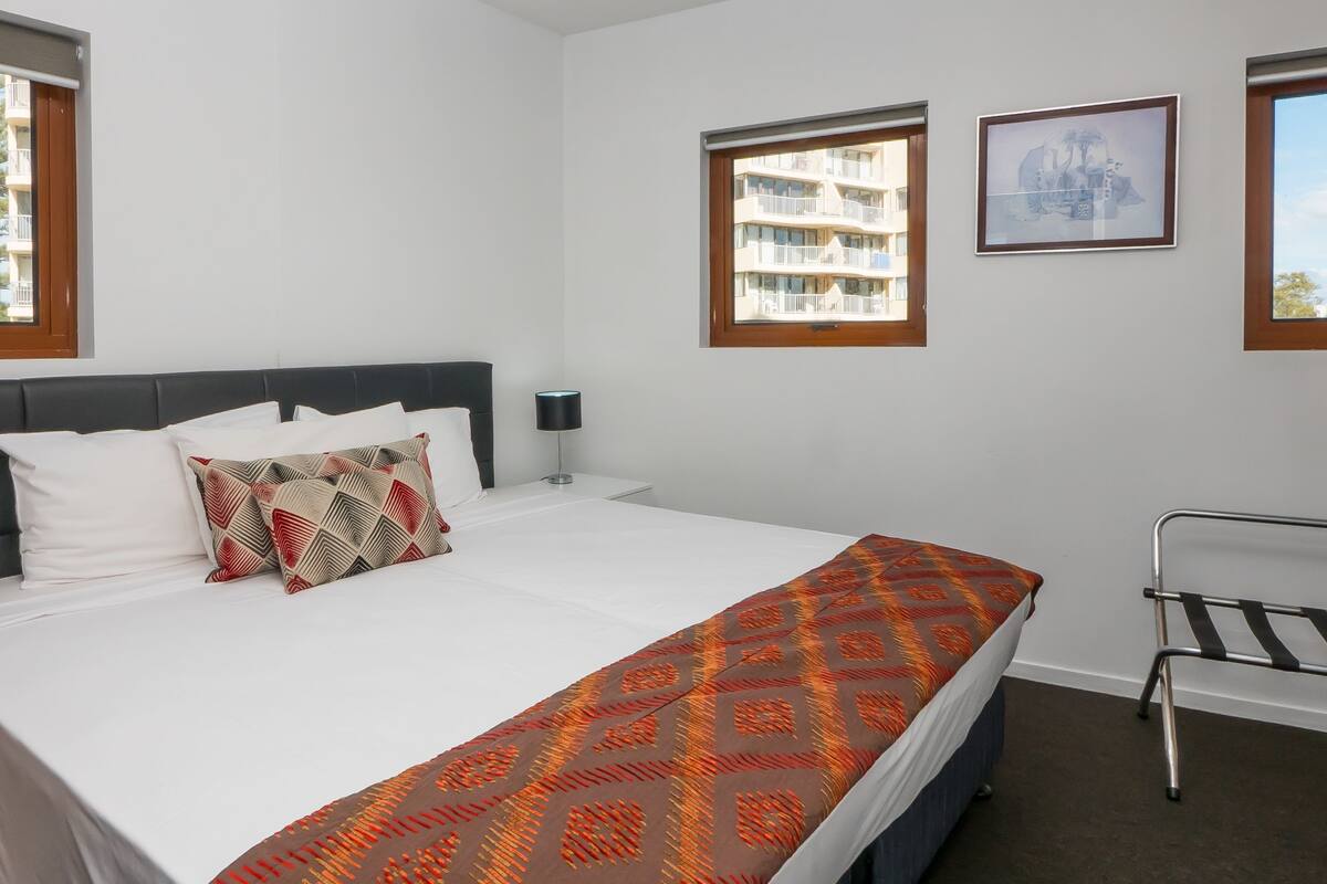 Een hotelkamer met een bed, bedlampje, telefoon, raam en een schilderij aan de muur.