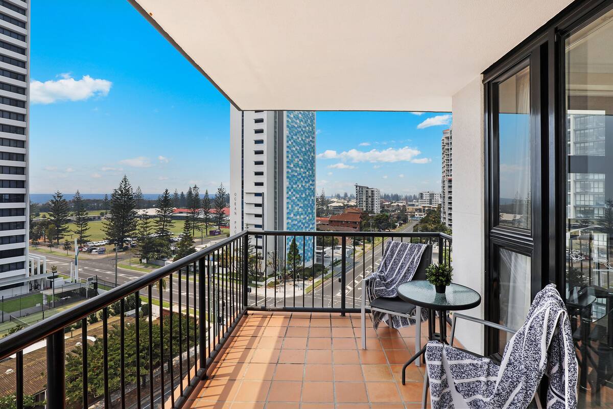 Un balcon avec un sol carrelé, deux chaises, une petite table et un pot de fleurs.
