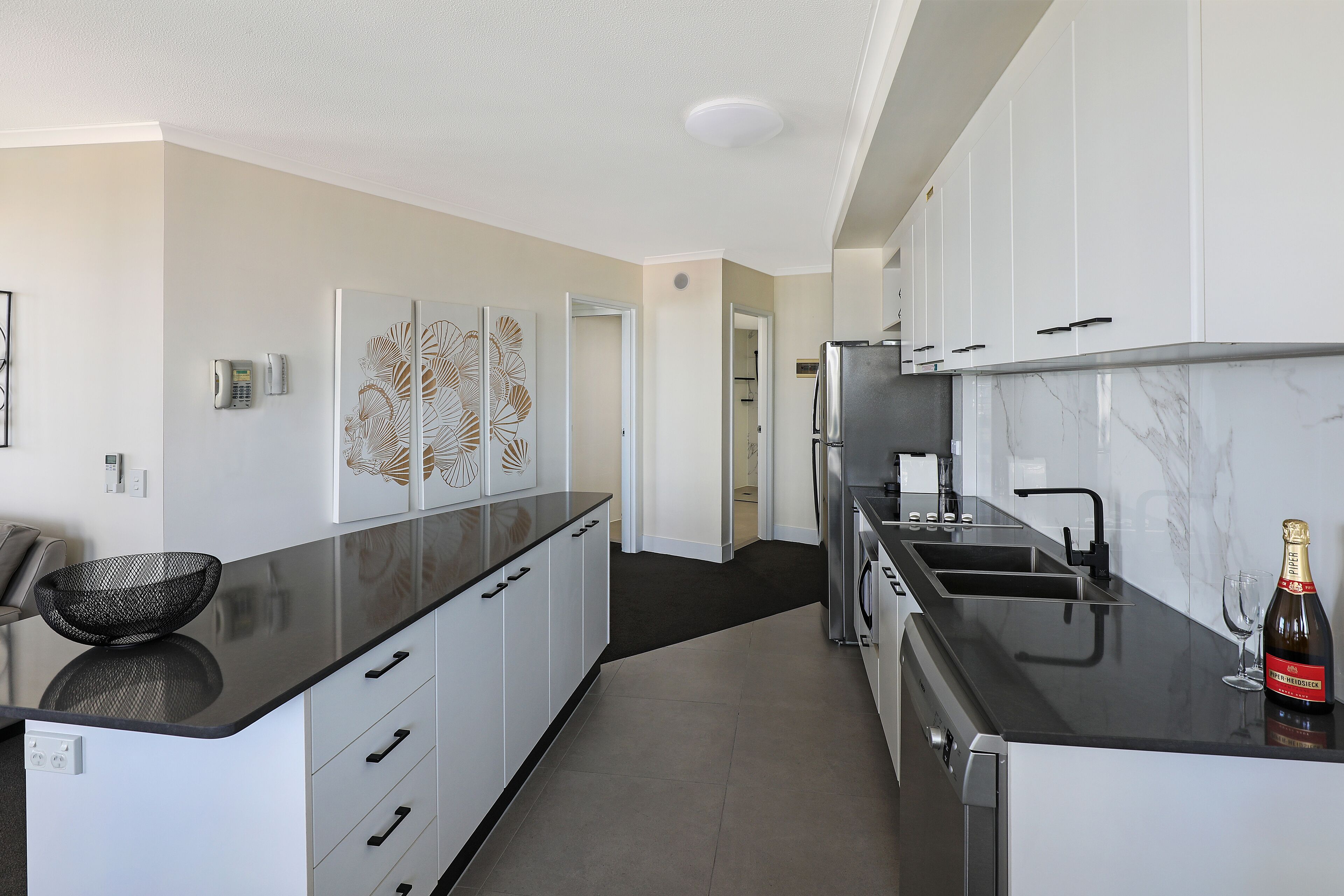 A modern kitchen with white cabinets, a black countertop, and a marble backsplash.