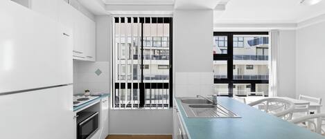 A modern kitchen with white cabinetry, a built-in oven, a large window with black bars, and a blue countertop.