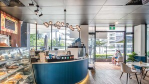 Ein modernes Café-Interieur mit einer blauen Theke, einer Glastheke voller Gebäck und Blick auf die Stadt durch große Fenster.