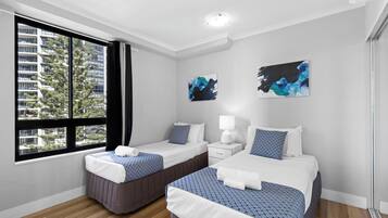 A hotel room with two beds, a window with curtains, a nightstand, and artwork on the wall.