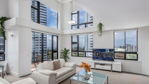 Ein geräumiges Wohnzimmer mit großem Fenster, einer Couch, einem Couchtisch und einem Fernseher.