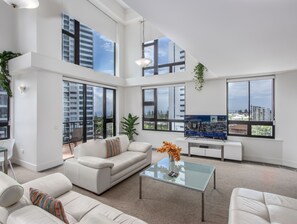 A spacious living room with a large sofa, a glass coffee table, and a TV. - Neptune Resort (Broadbeach)