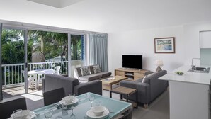 A modern living room with a dining area, a flat-screen TV, and a balcony with a view of palm trees. - BreakFree Diamond Beach (Mermaid Beach)