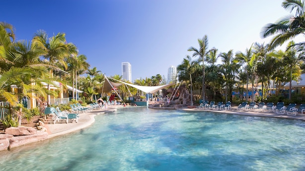 A clear pool with lounge chairs and palm trees, surrounded by buildings. - BreakFree Diamond Beach (Mermaid Beach)