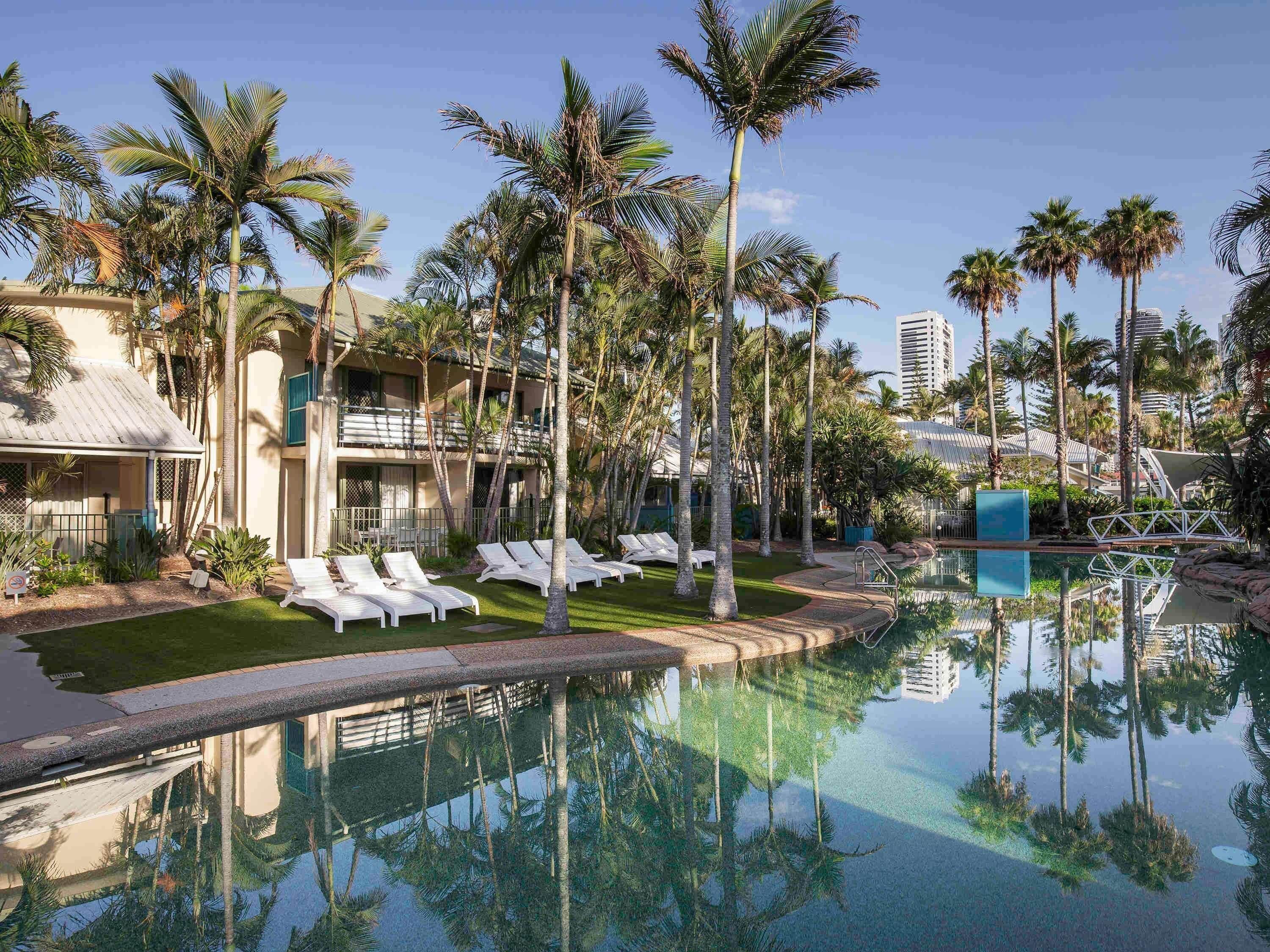 Un resort con piscina, palmeras y sillones de descanso.